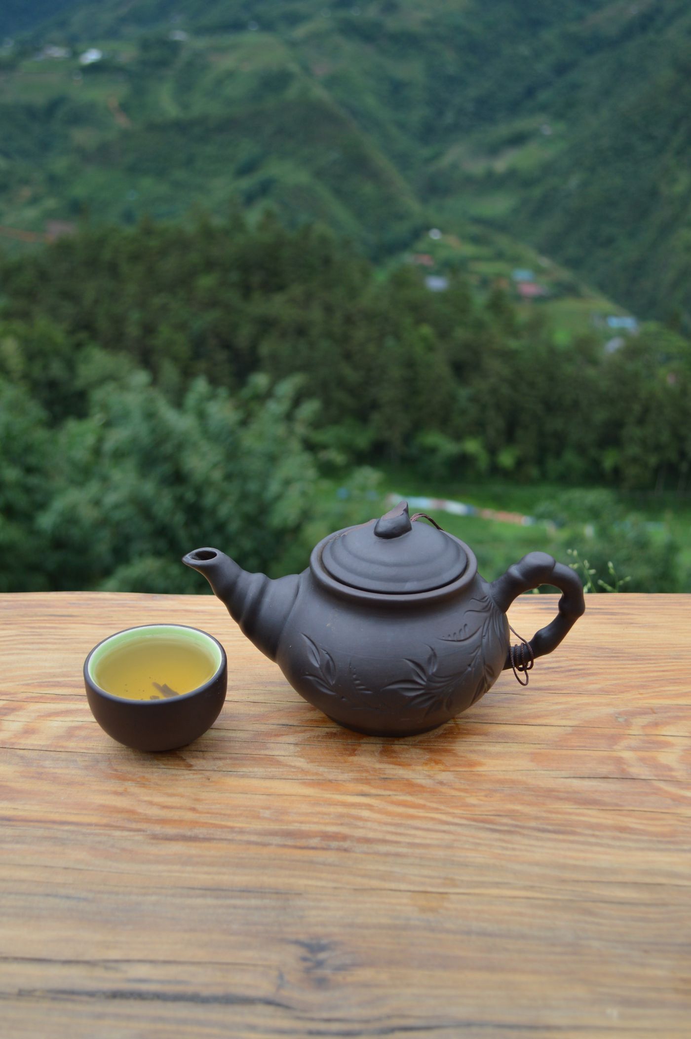木桌上的深色陶壶与茶杯，背景是山谷